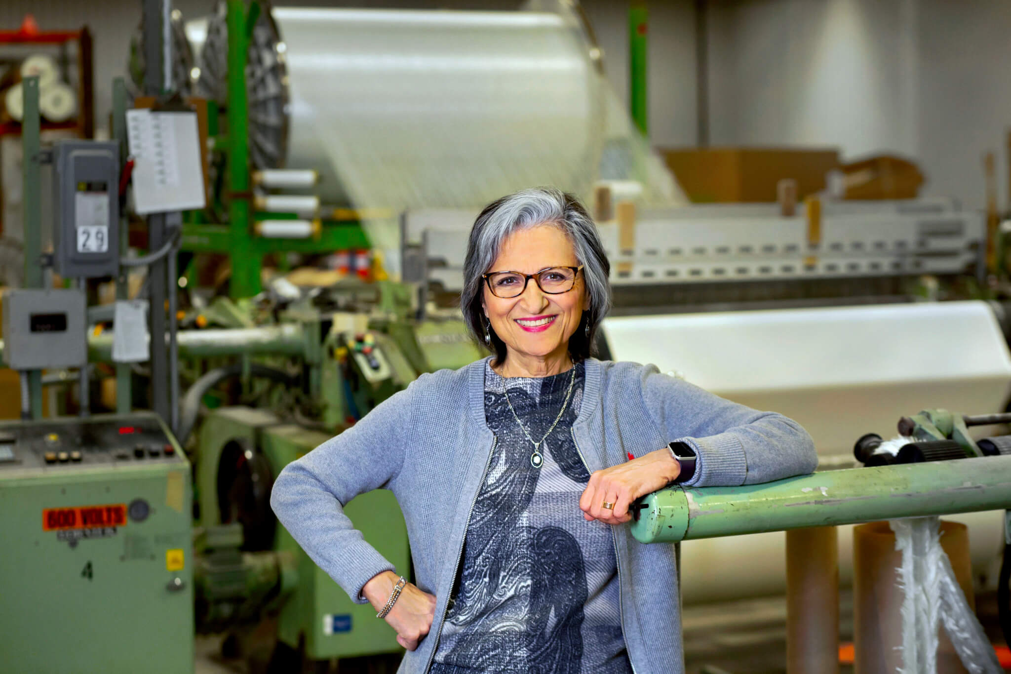 Kathie Leonard smiles, leaning on a post, in front of manufacturing equipment